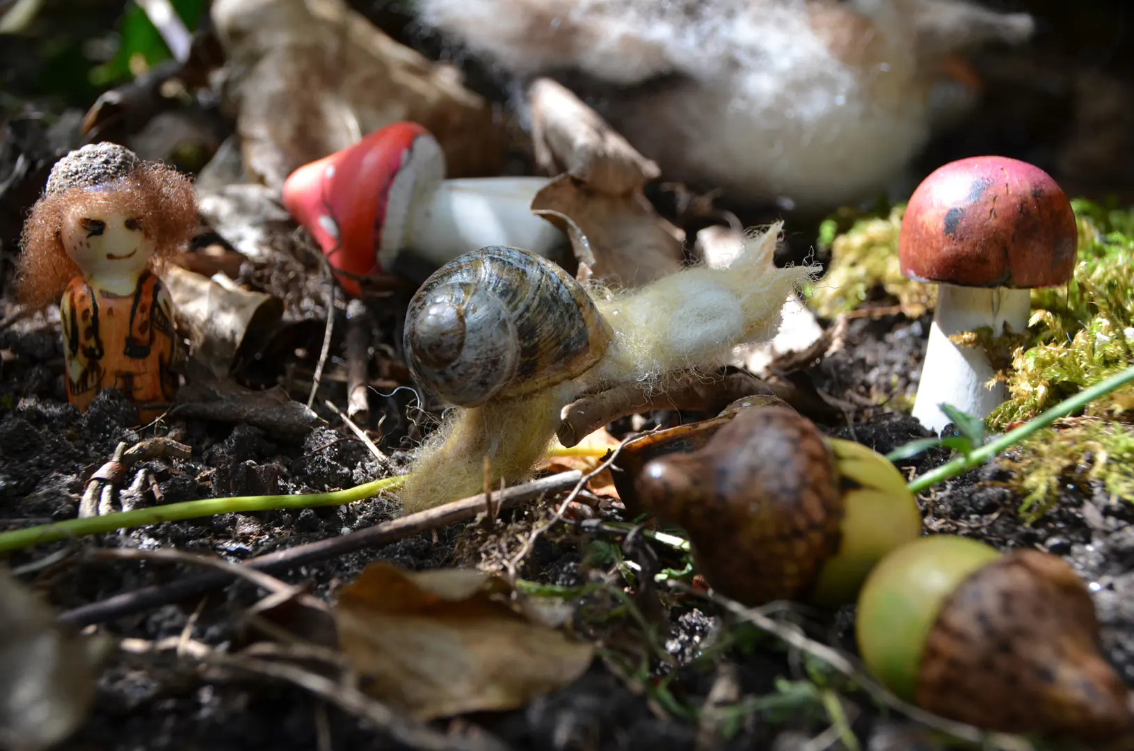 Een verzameling handgemaakte seizoensdecoratie met houten paddenstoelen, eikeltjes en een naaldvilten slakje met een echt huisje. Aan de zijkant komt stiekem een houten peg doll boskindje met schapenwol en eikelhoedje om de hoek kijken. Een speelse en complete set voor de herfstachtige seizoenstafel.