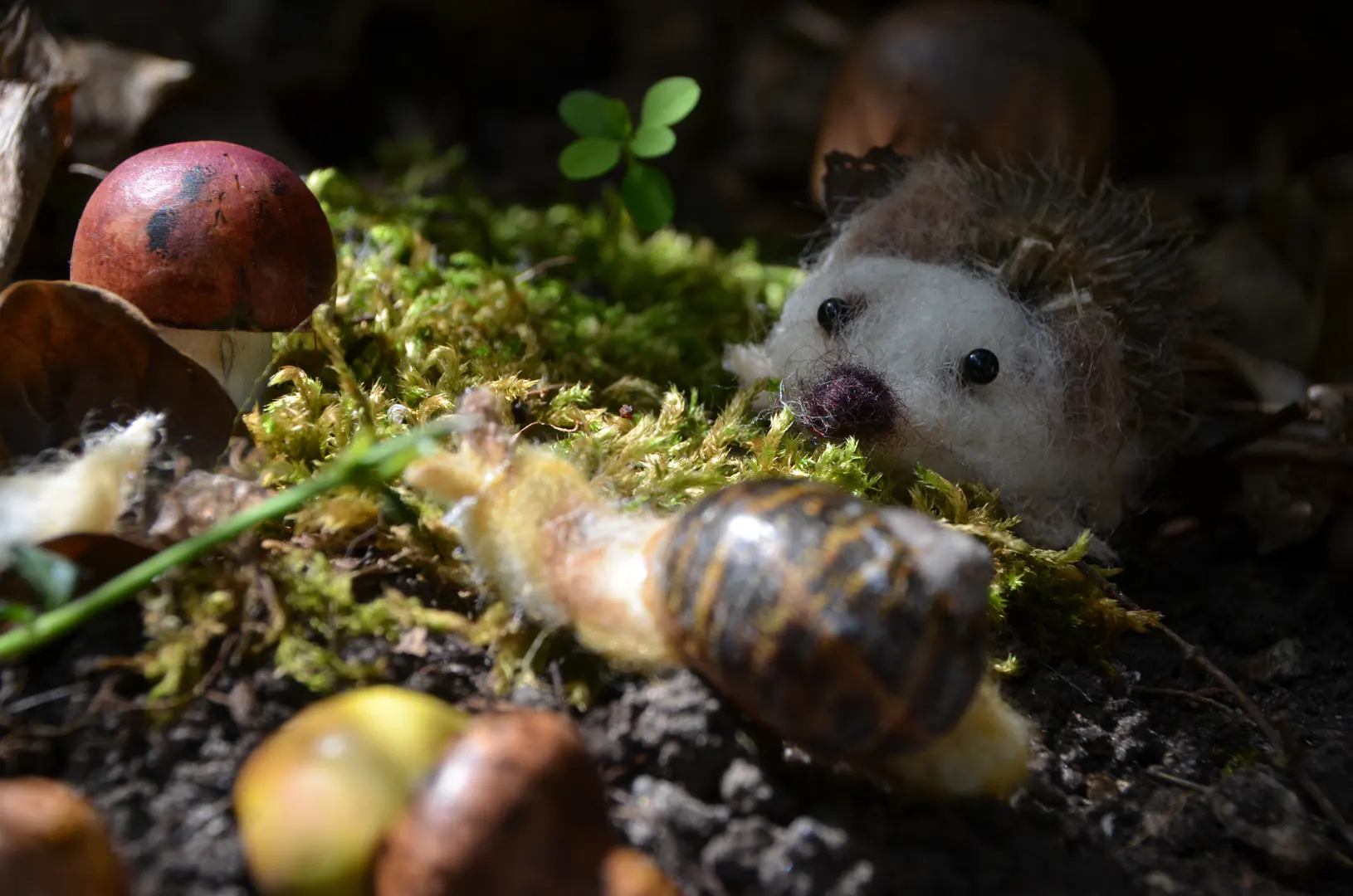 Sfeervol herfsttafereel op de mosgrond, prachtig uitgelicht door warme zonnestralen. Handgemaakte houten eikeltjes, een paddenstoeltje en vilten diertjes zoals een egeltje en slakje smelten hier naadloos samen met de natuurlijke omgeving.