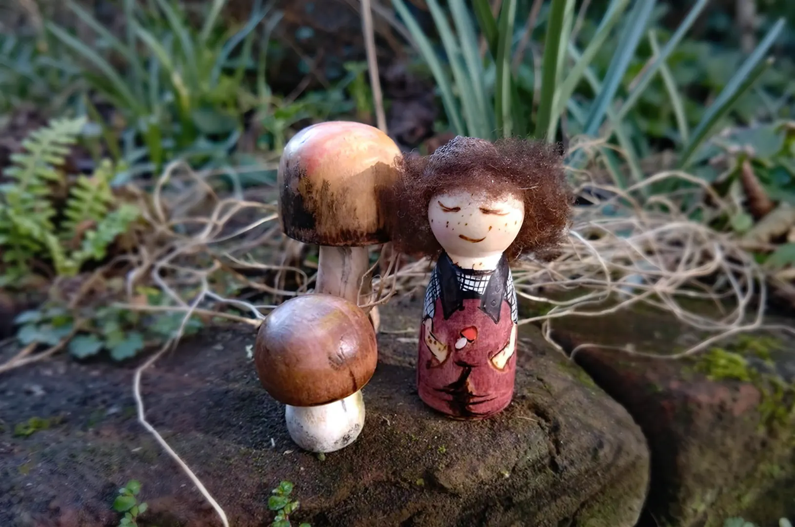 Handgemaakt houten peg doll boskindje, vergezeld door twee houten paddenstoelen. Liefdevol beschilderd en afgewerkt met pure, onbewerkte lokale schapenwol. Een warm en natuurlijk herfsttafereel.